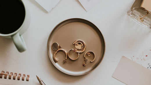 Gold-plated hoops in a ceramic dish on a desk beside a mug and pen