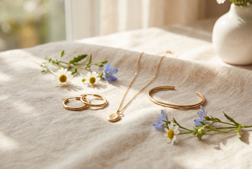 Gold-plated hoop earrings, pendant and bracelet on linen among daisies and blue wildflowers