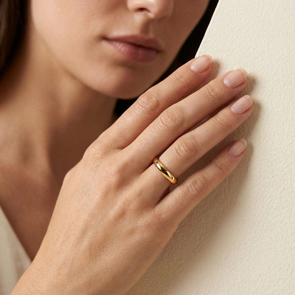 Smooth gold-plated ring on a model's finger against a light wall