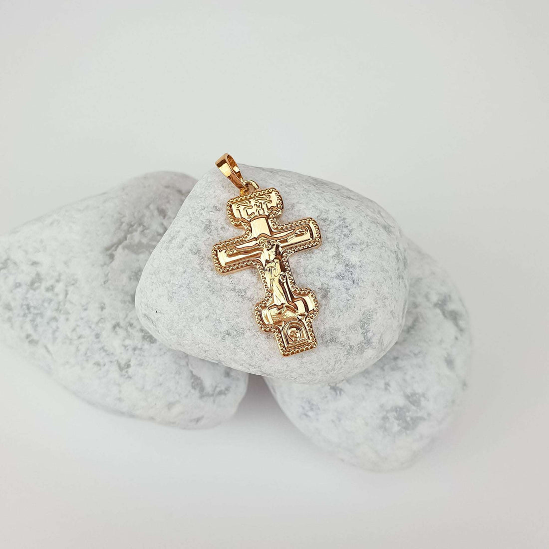 Gold-plated eight-pointed Orthodox cross pendant with Christ figure and fine engraving, lying on pebbles
