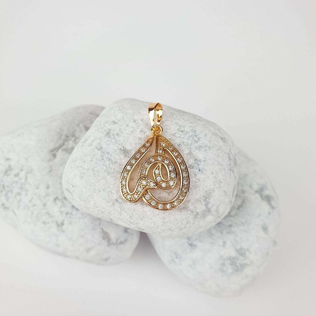 Snake pendant at an angle on pale pebbles, gold-tone with white cubic zirconia