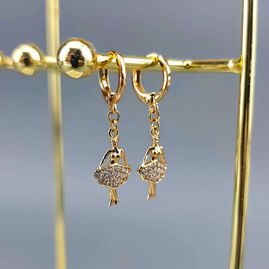 Gold-plated ballerina drop earrings with cubic zirconia skirts on a gold jewellery stand