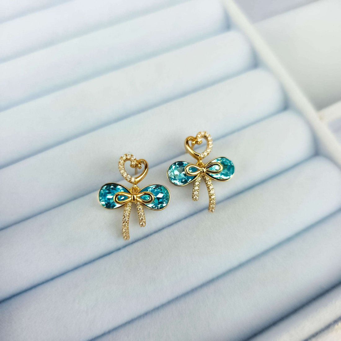 Bow earrings with bluish stones in a light jewellery box, warm gold tone