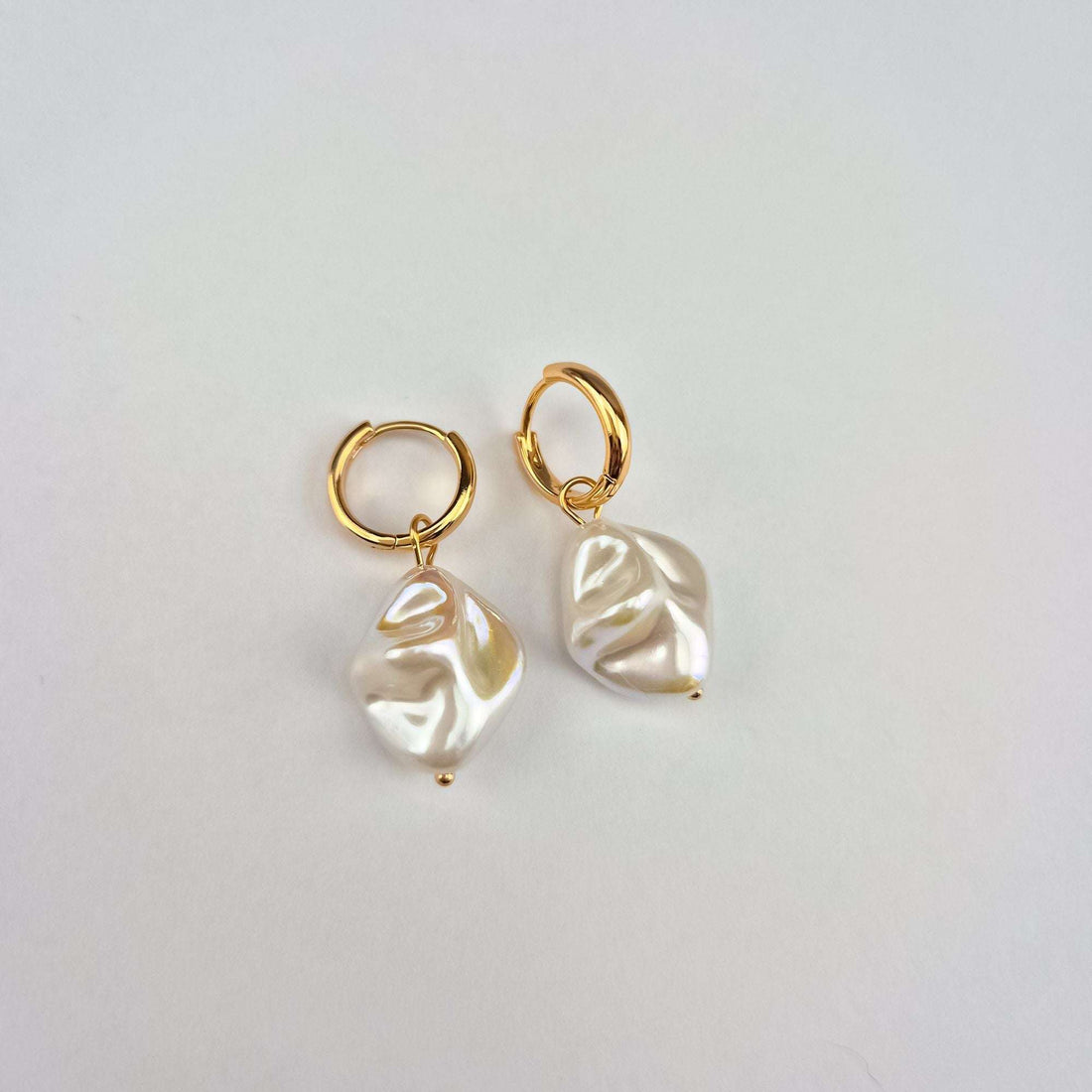 Close-up of gold-plated hoop earrings with faux pearl drops on light fabric