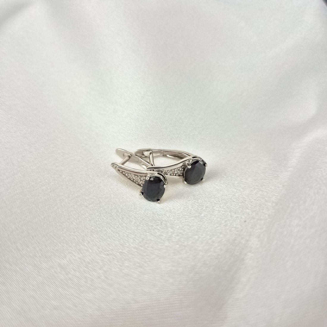 Silver-tone black stone earrings on white silk, leverback clasp visible