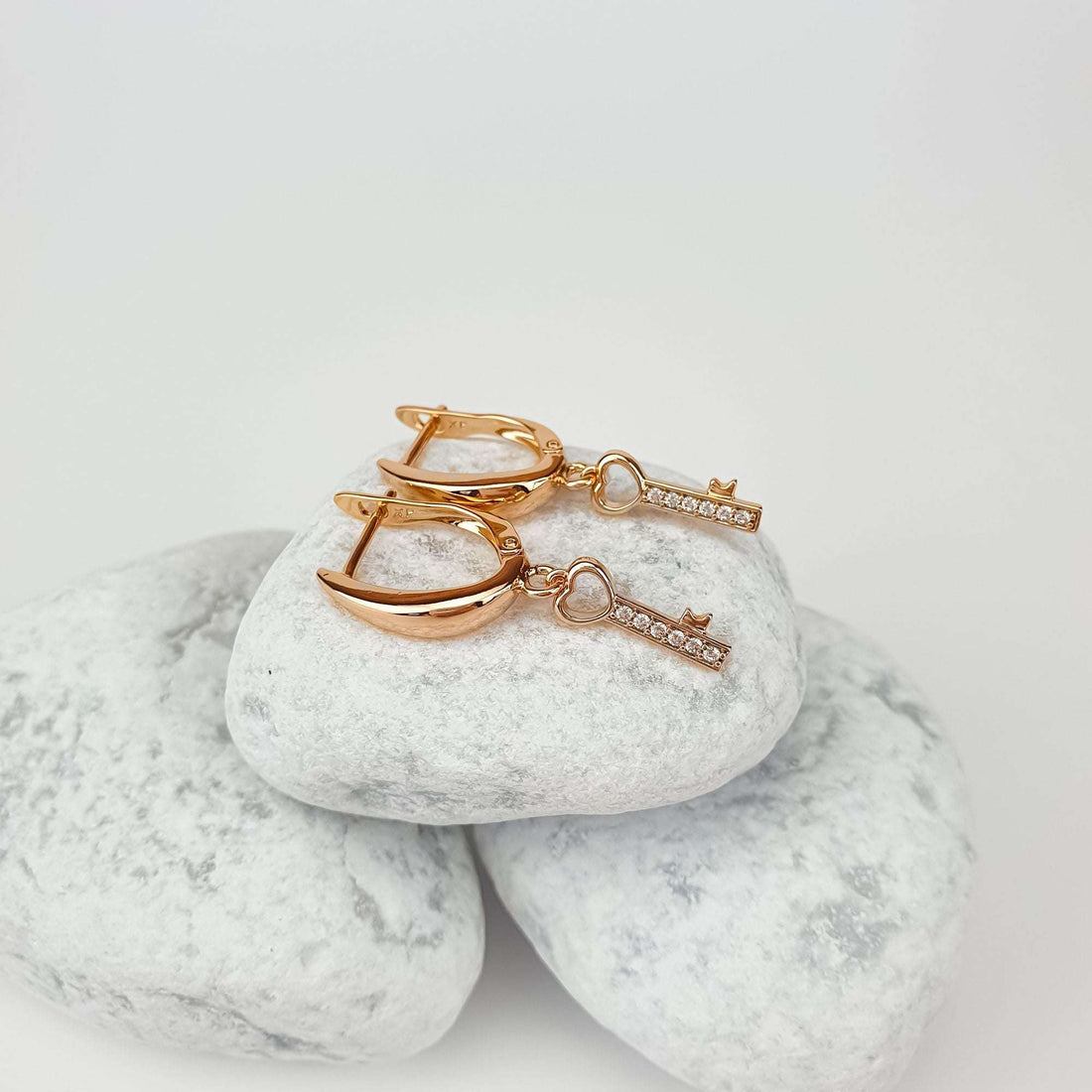 Pair of key earrings in side view on white pebbles, gold-plated leverback visible