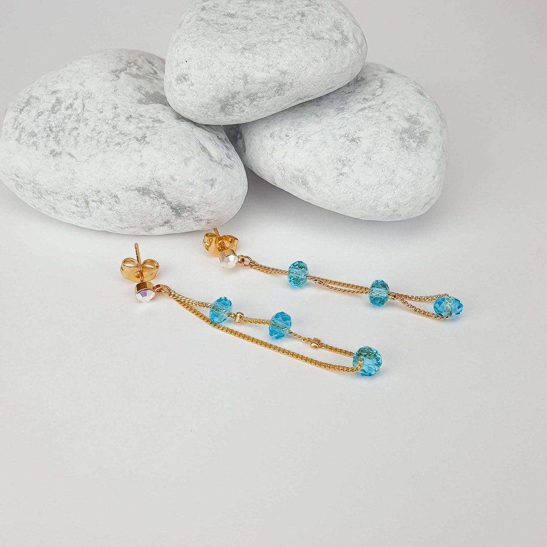 Pair of gold-plated earrings on light stones with visible posts and blue crystals