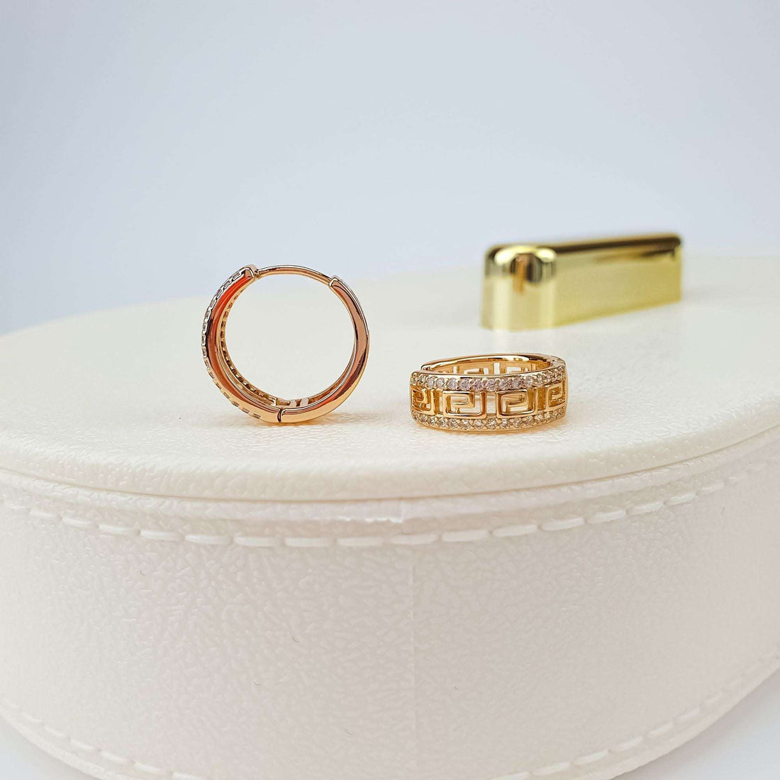 Openwork Greek pattern earrings on a white jewellery box, close-up