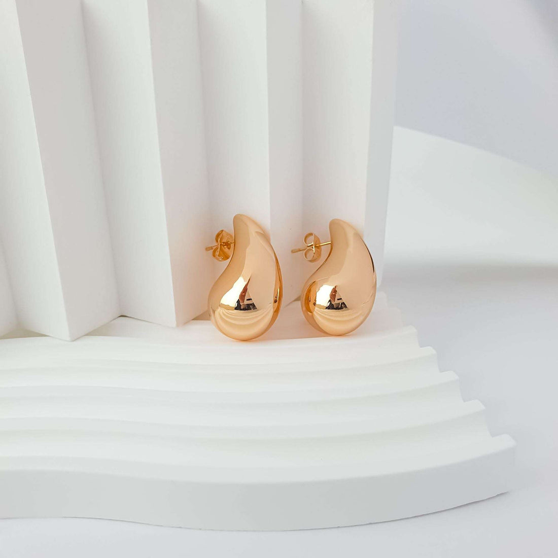 Gold-tone teardrop earrings from the side on a white stand, push-back post visible