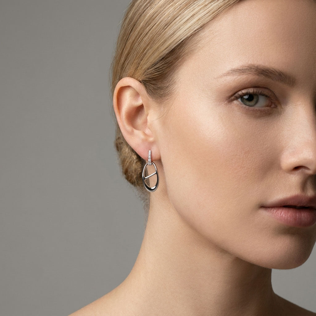 Model wearing oval silver-tone earrings with a stone bar, grey background