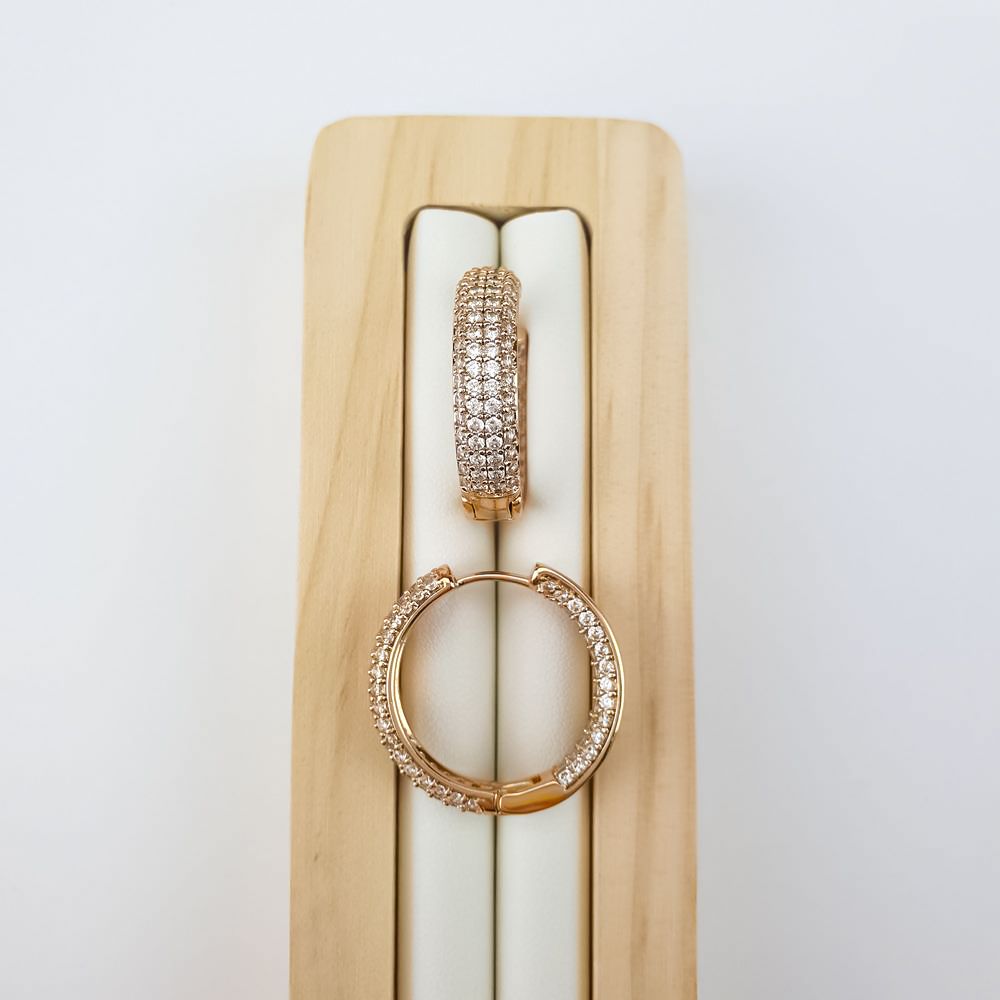 Gold-plated hoop earrings covered with clear cubic zirconia on a light wooden tray
