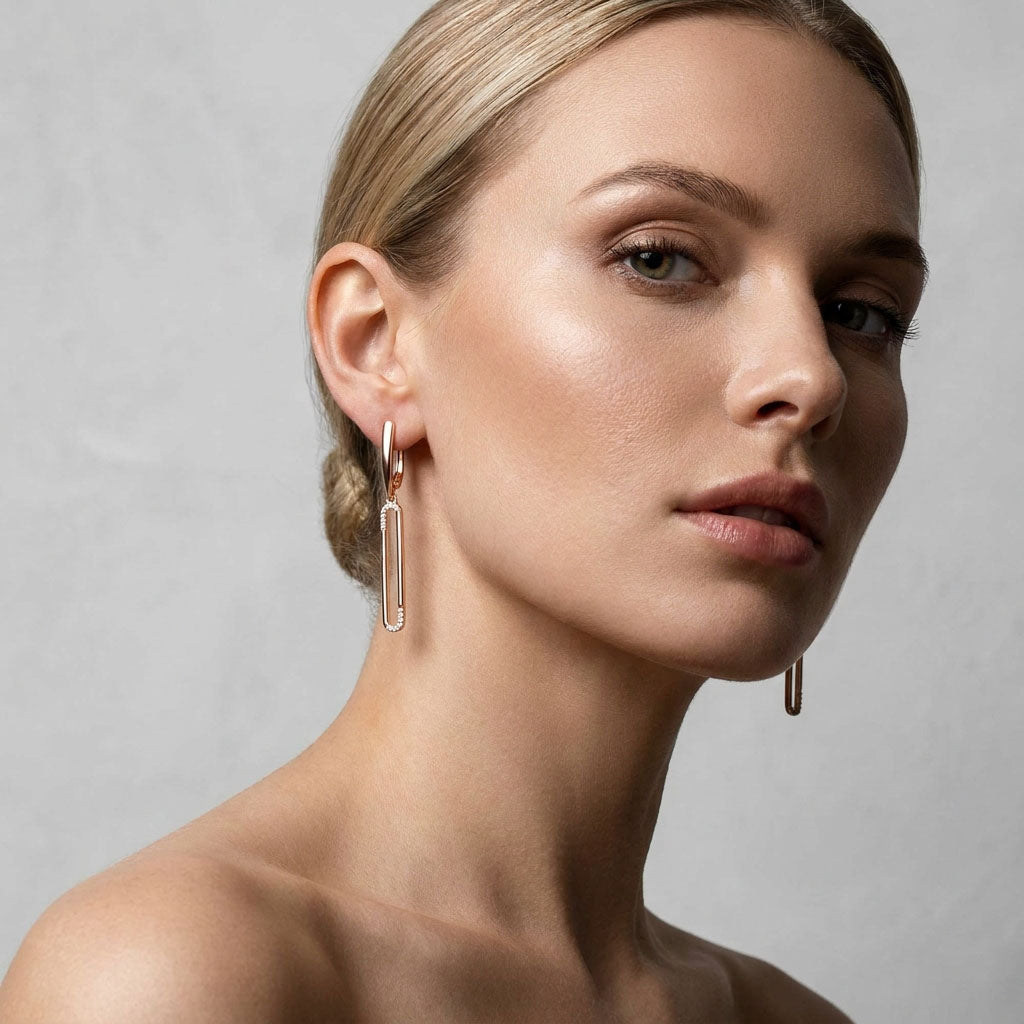 Model in profile wearing long gold-plated oval earrings, light grey background