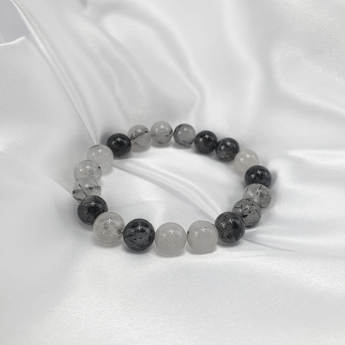 Black and white tourmalinated quartz bracelet on white satin, glossy round beads