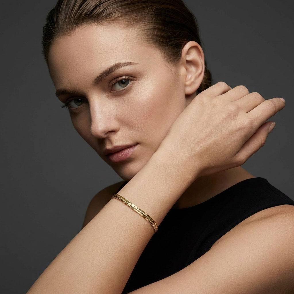 Model in a black top wearing the gold-plated woven bracelet, dark background