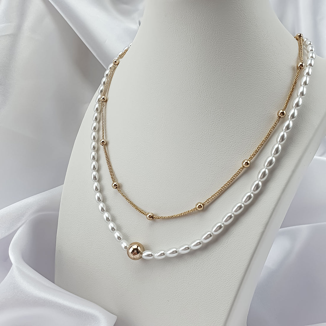 Pearl necklace with a gold-plated ball chain on a white bust, close-up