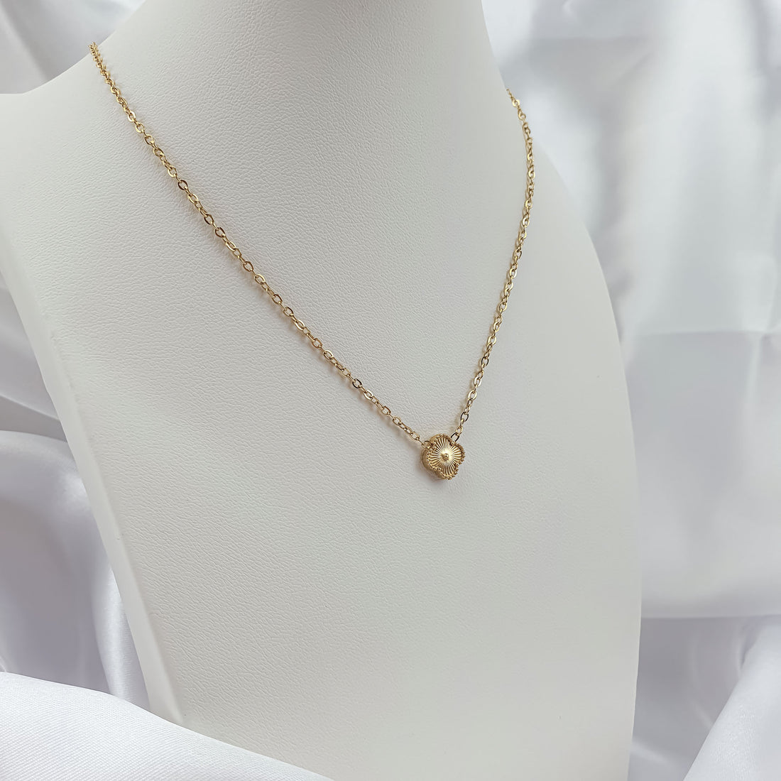Gold-plated clover necklace with a ray pattern on a white bust