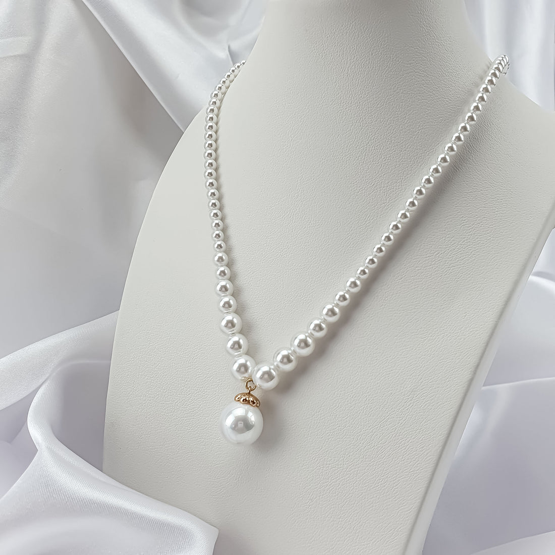 Pearl necklace on a white stand against satin, pearl drop with a gold-tone cap