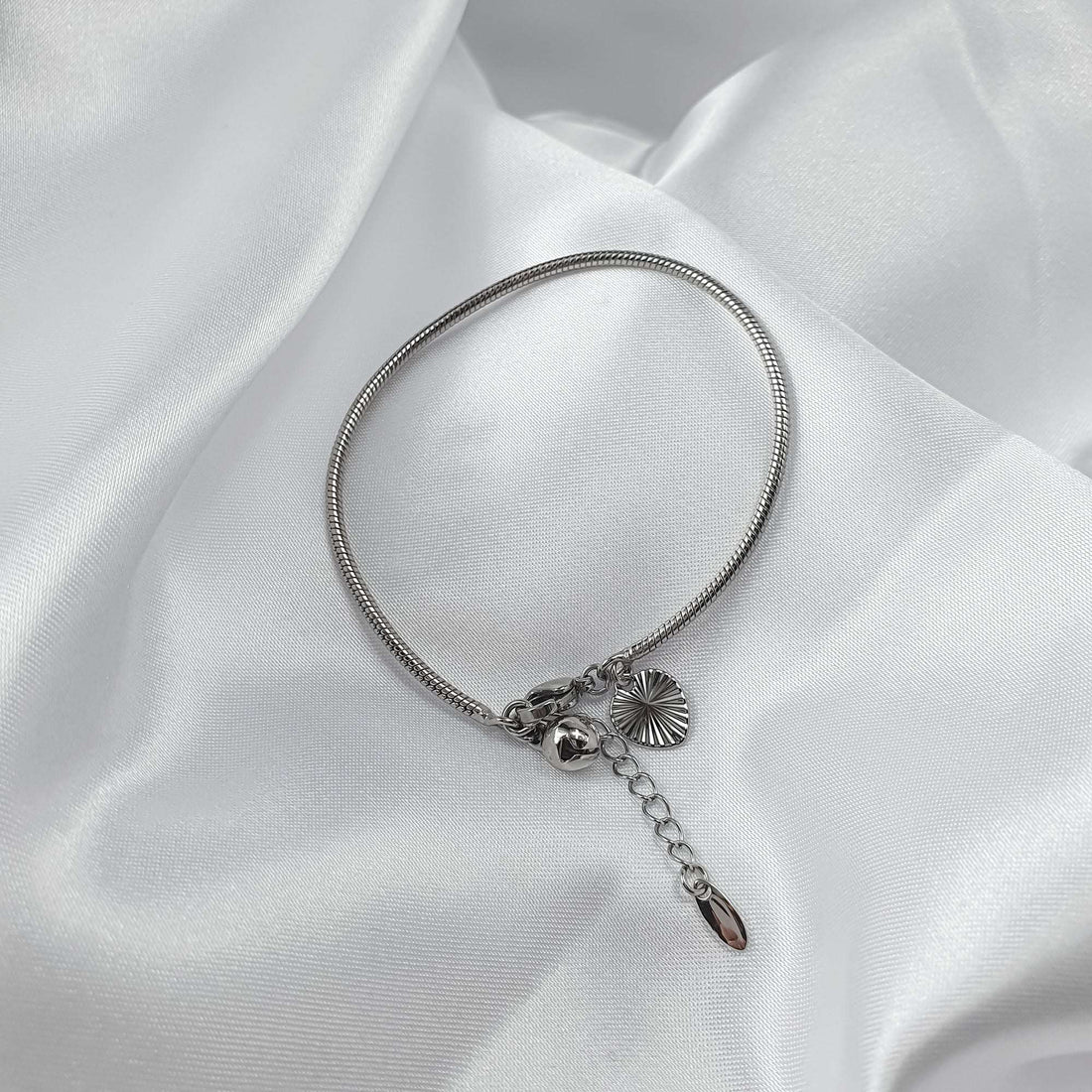 Bracelet on white silk, close-up of ribbed heart, round bell and lobster clasp