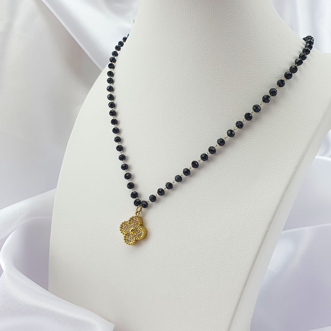 Stone-set gold-plated clover pendant on a black bead necklace, white bust