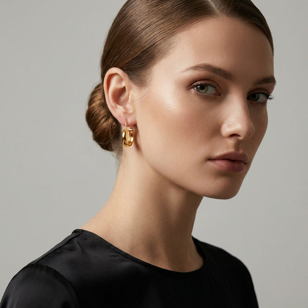 Model wearing a thick gold-tone hoop earring with a black blouse