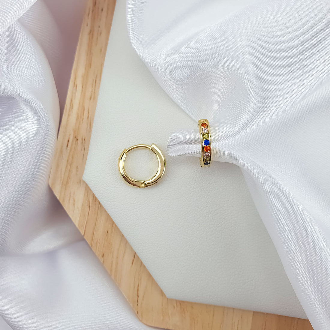 Hoop earrings with colourful stones on a pale leather pad and wooden board