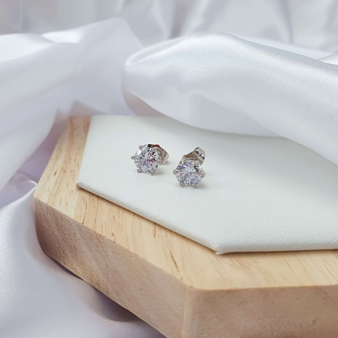 Two silver-tone cubic zirconia studs at an angle on a white tray, posts visible