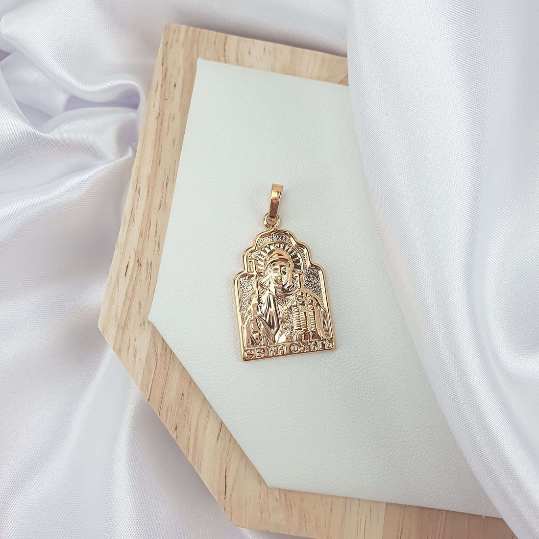 Gold-plated icon pendant on a light wooden board with fabric