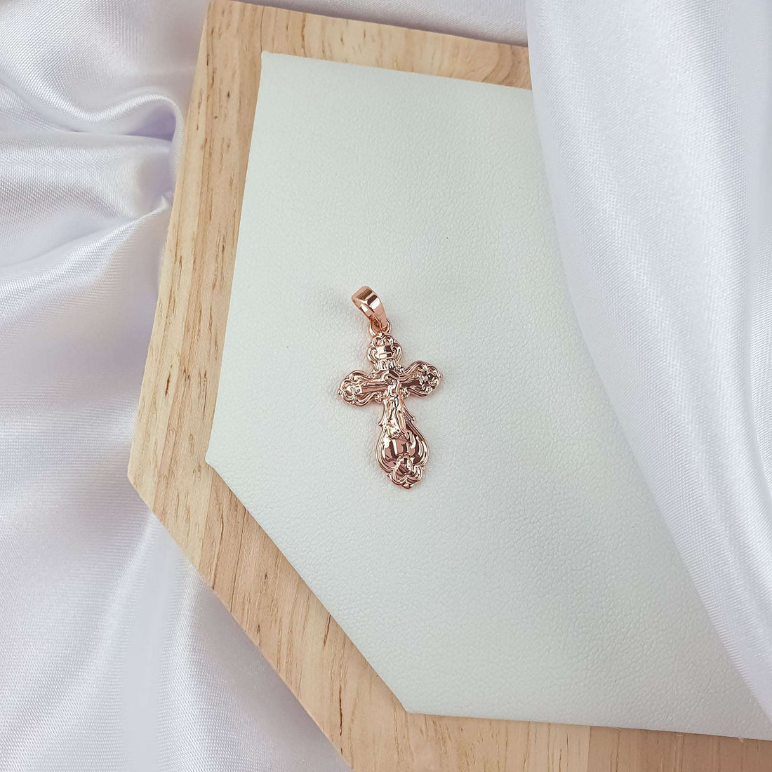Delicate rose gold-plated cross on a wooden board and white silk