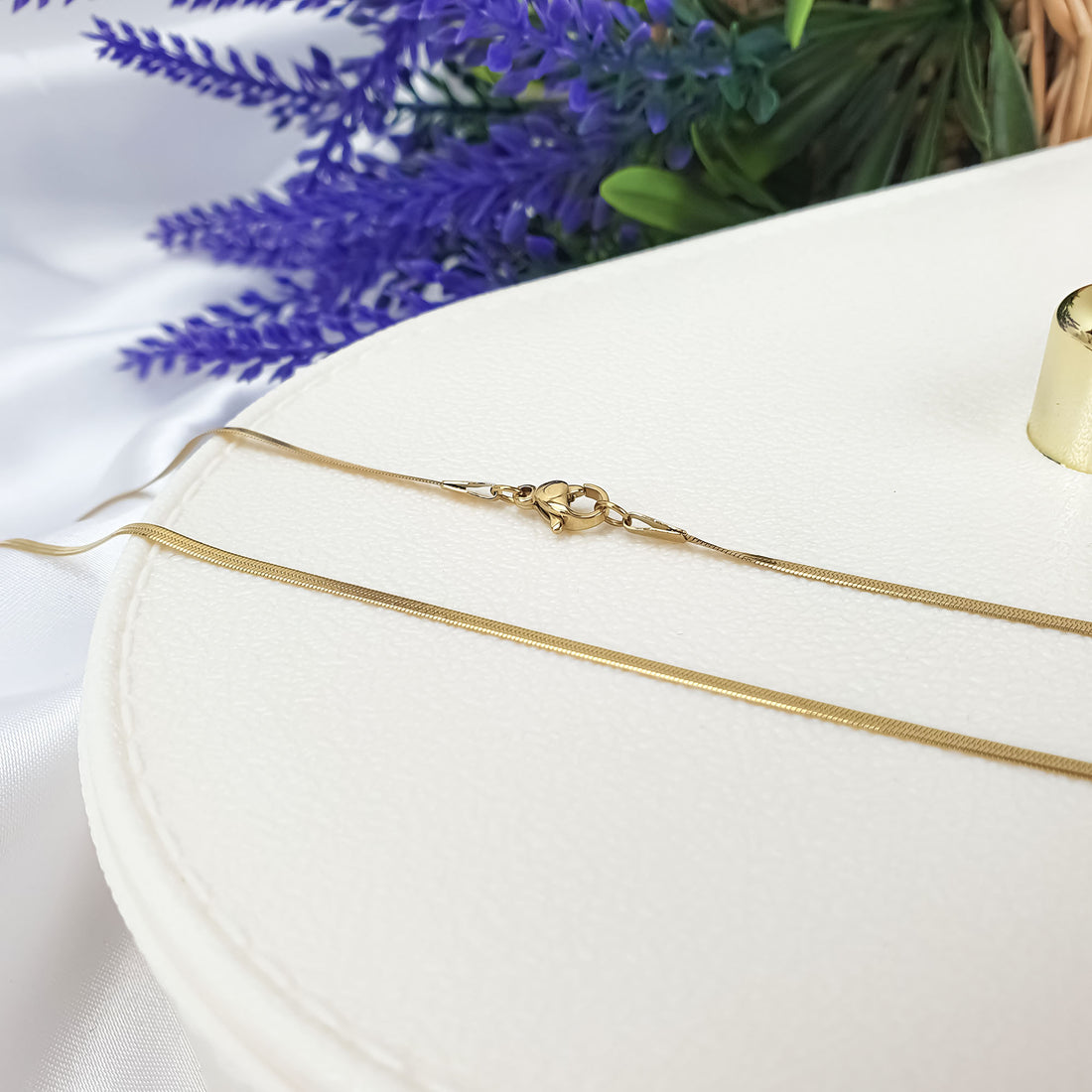 Thin gold-plated snake chain with clasp on a light box beside lavender