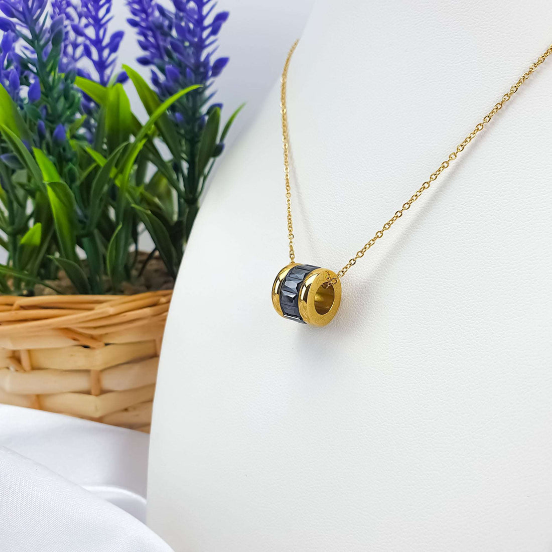Gold-plated chain with a cylinder pendant and faceted black stones on a display bust