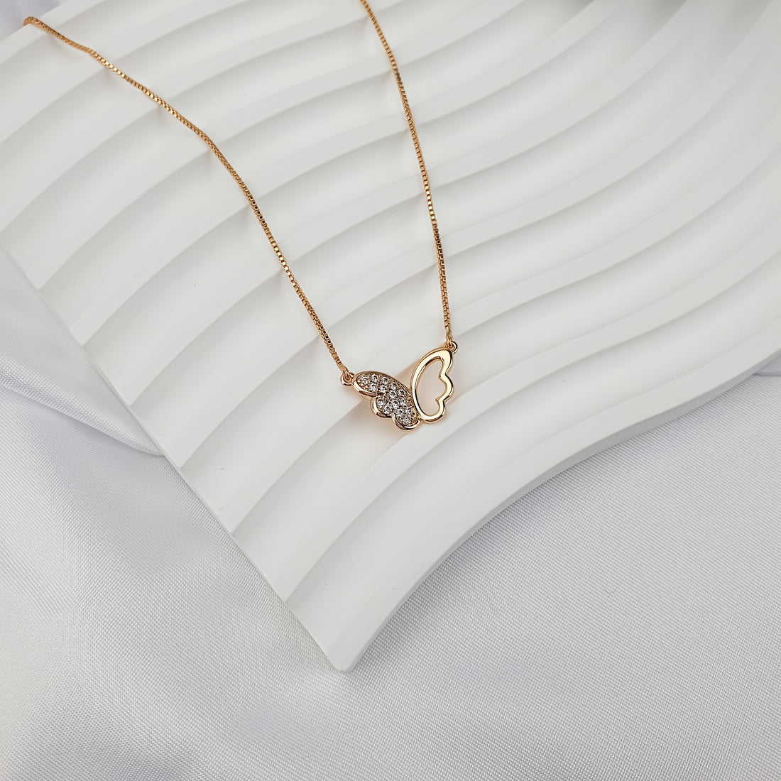 Gold-plated butterfly pendant with a cubic zirconia wing on a wavy white ceramic tray