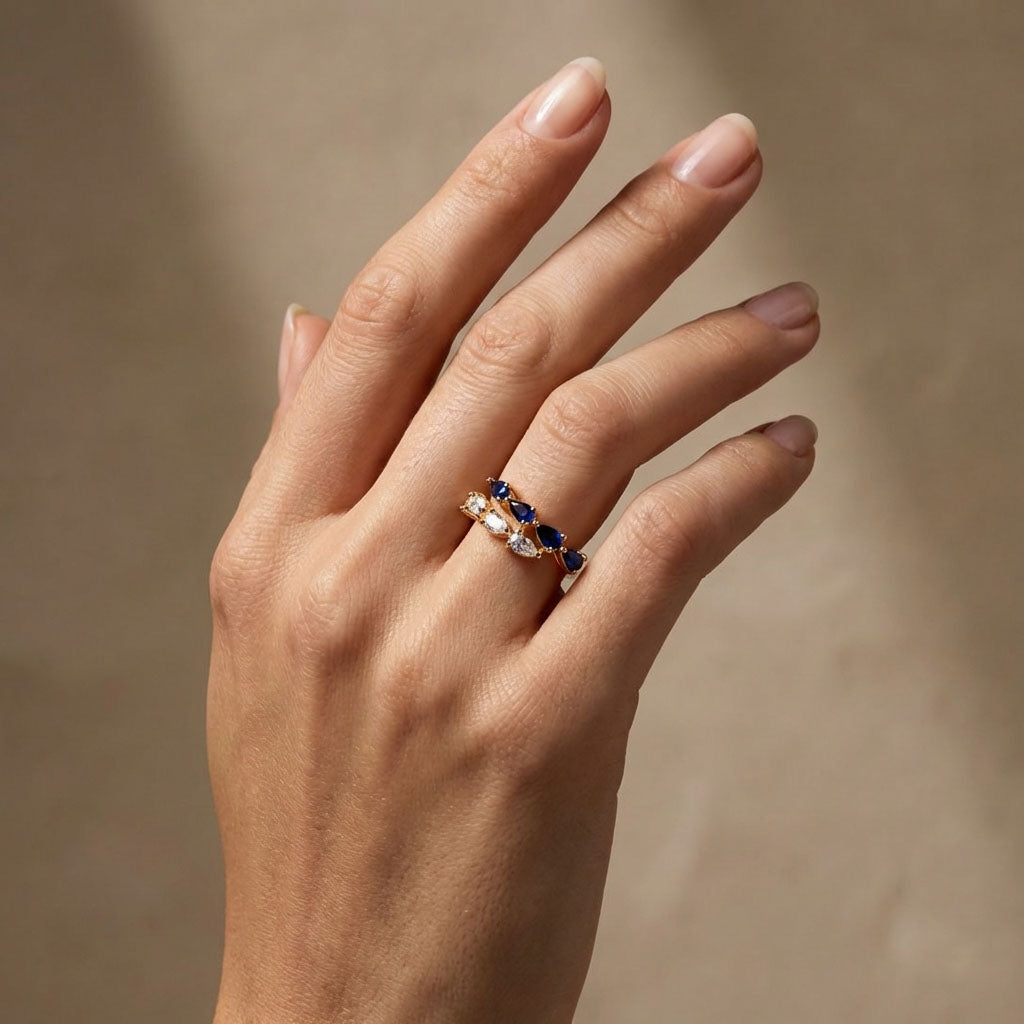 Model wearing a gold-plated ring with blue and clear teardrop cubic zirconia