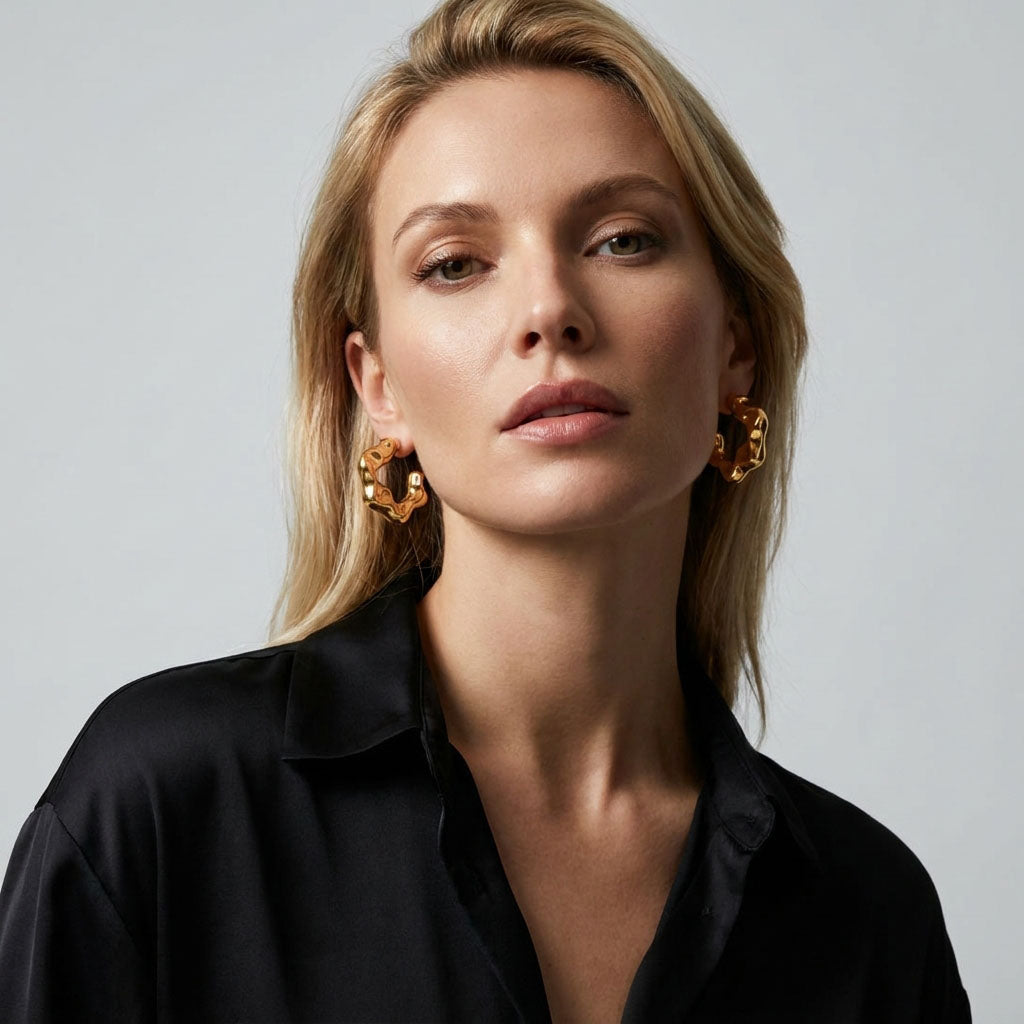 Model in a black shirt wearing wavy gold-tone hoop earrings, close-up portrait