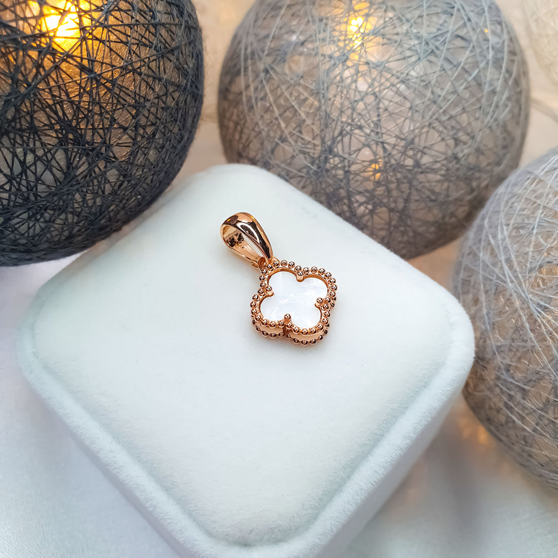 Gold-plated clover pendant on a white velvet box with warm lights