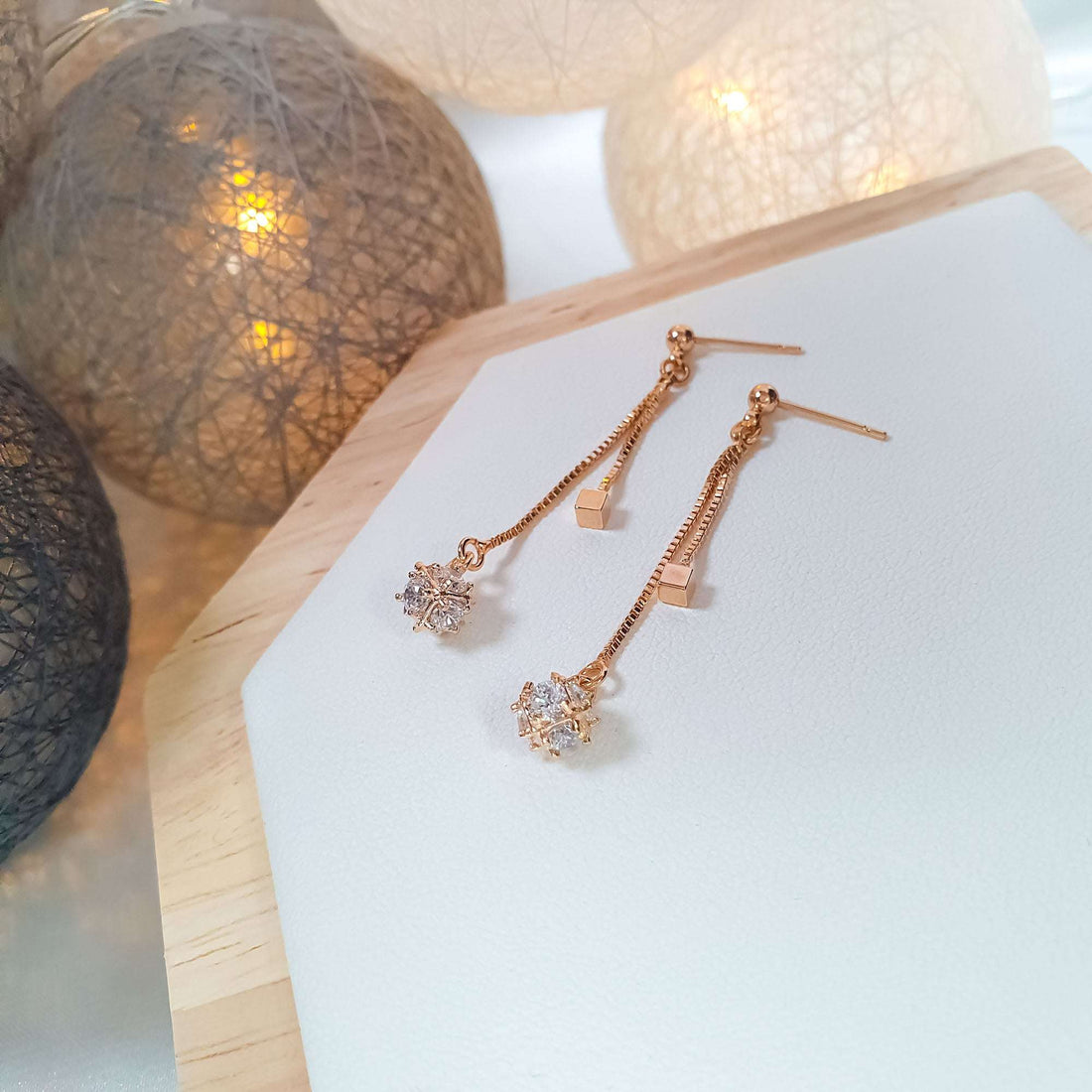 Chain drop earrings with clear stones on a light wooden stand