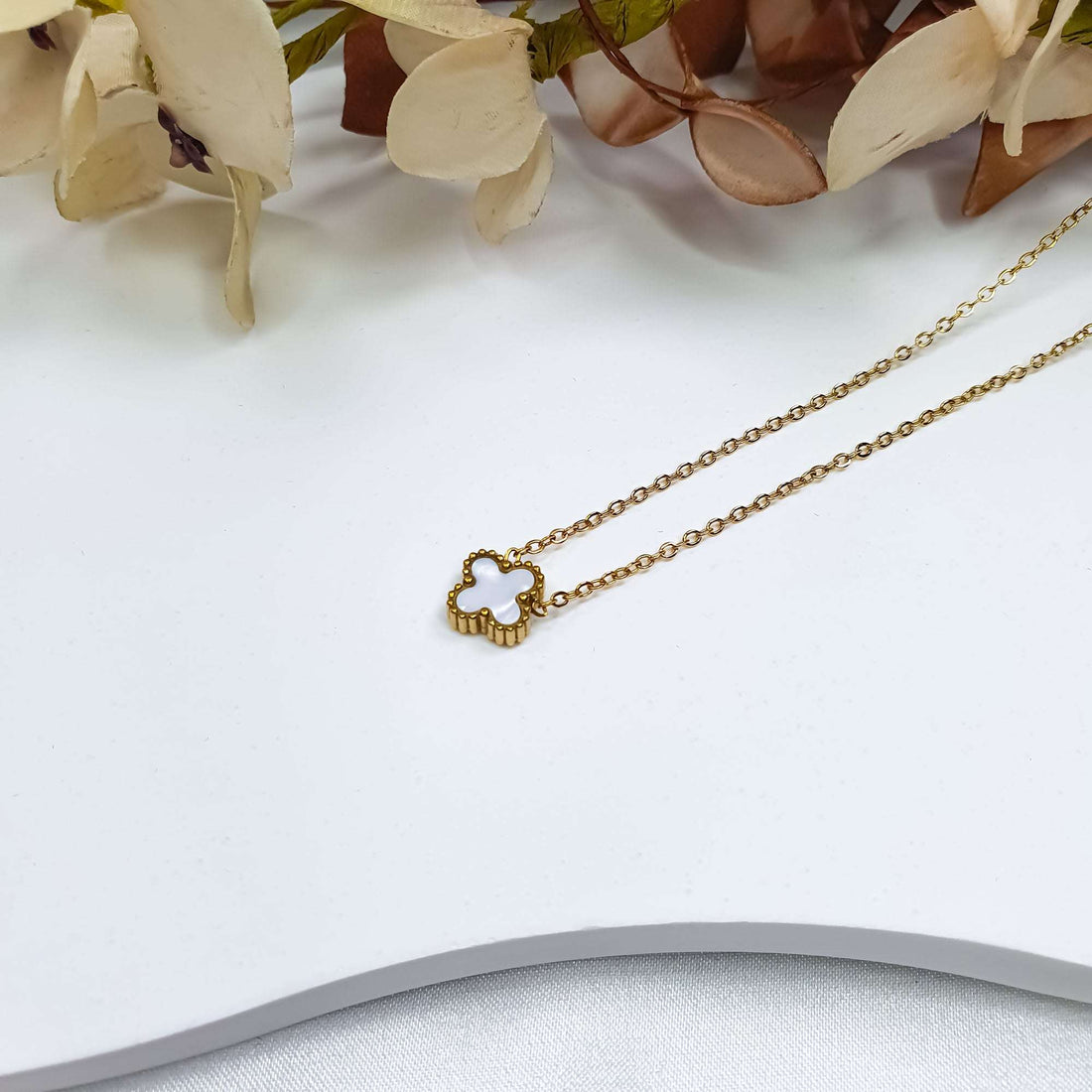 White clover pendant close up with a gilded beaded edge on a light surface