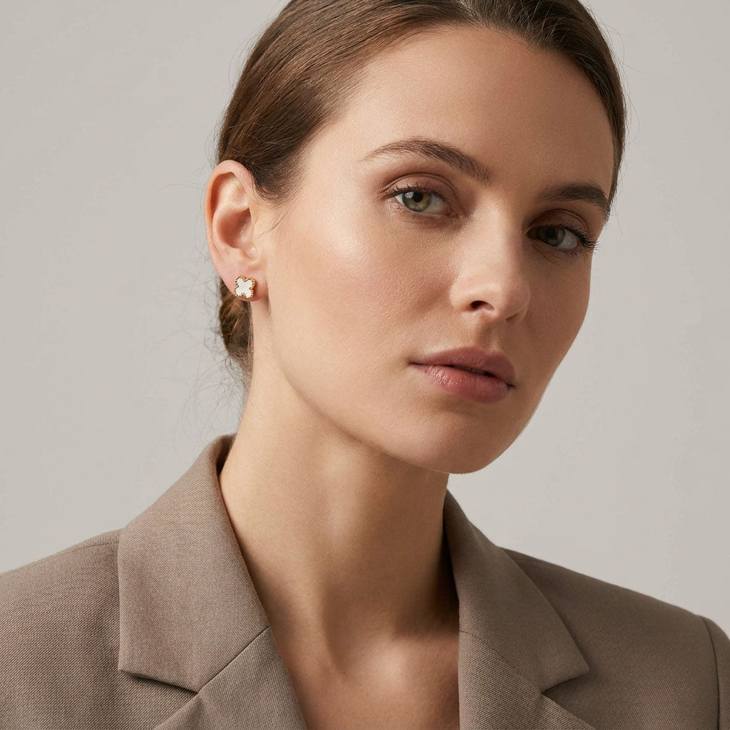 Model in a beige jacket wearing a small white clover stud in gold-tone frame