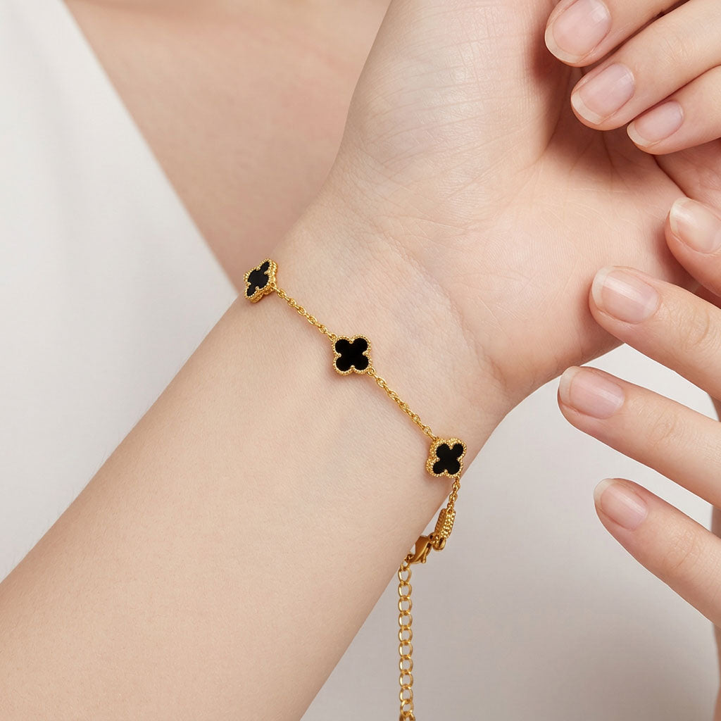 Black clover bracelet on a woman's wrist showing the fine gold-tone chain