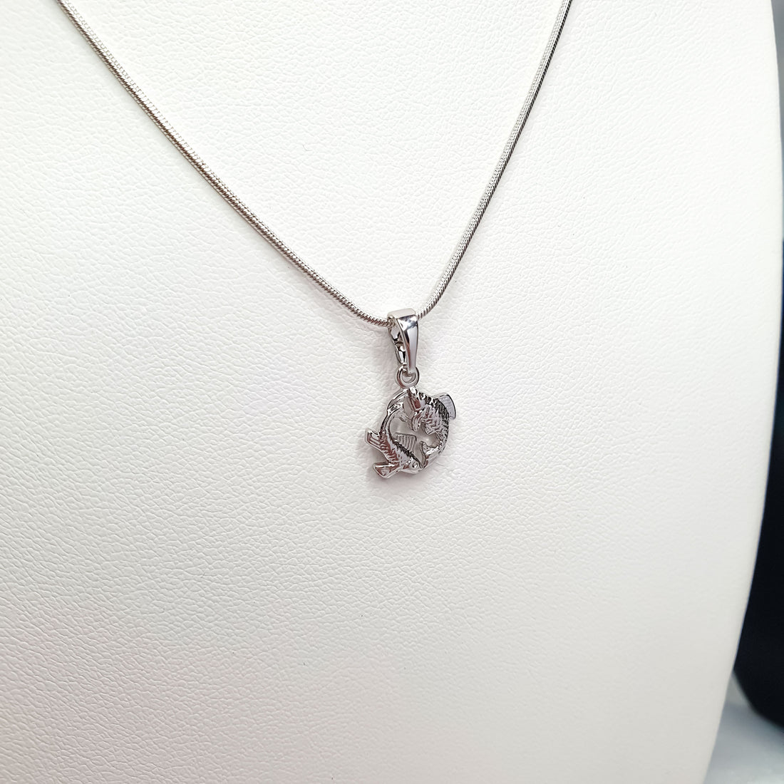 Silver-tone Pisces pendant hanging from a fine chain on a white jewellery stand