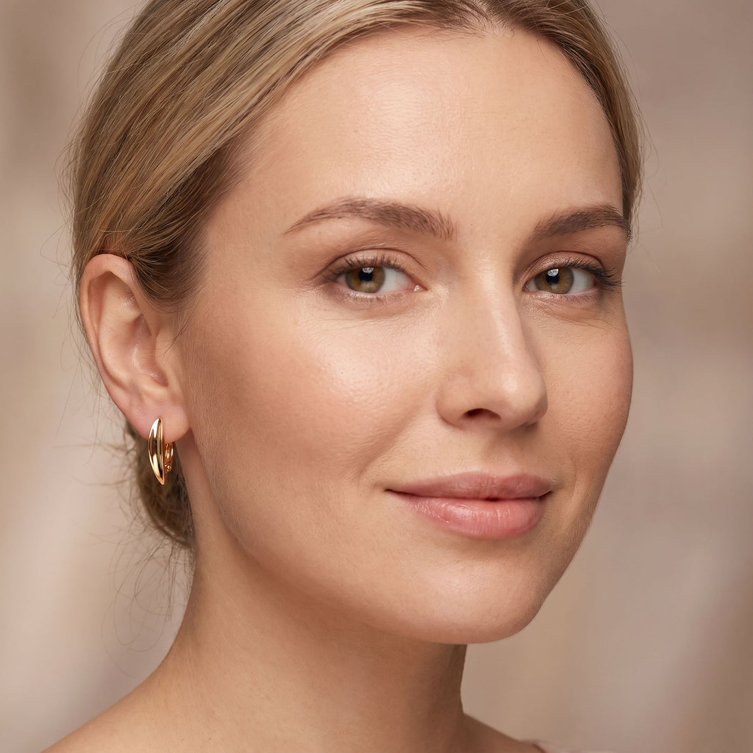 Gold | Close-up of a woman wearing smooth curved gold-tone earrings