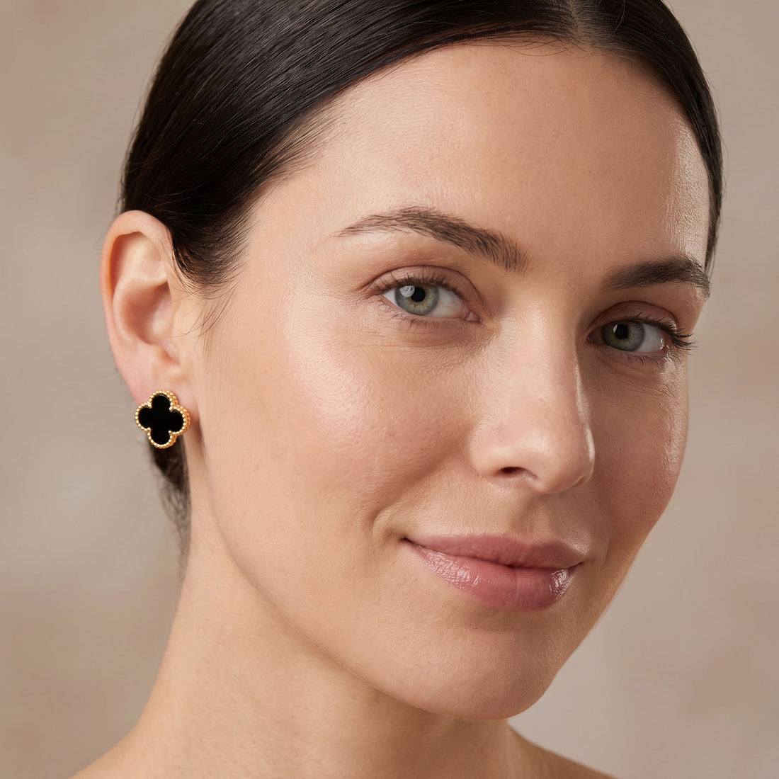 Woman wearing a black clover stud earring with gold-tone frame
