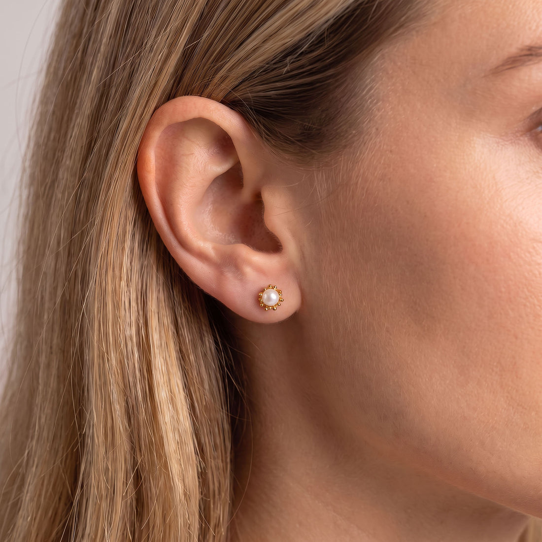 Gold-tone pearl flower stud earring worn on a woman's earlobe