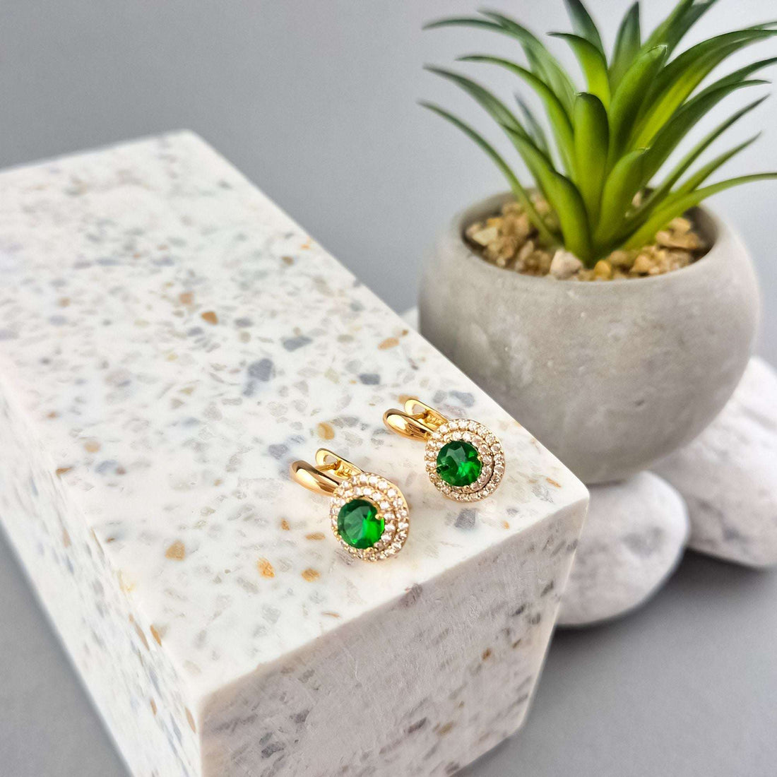 Green stone leverback earrings on a white terrazzo block beside a plant
