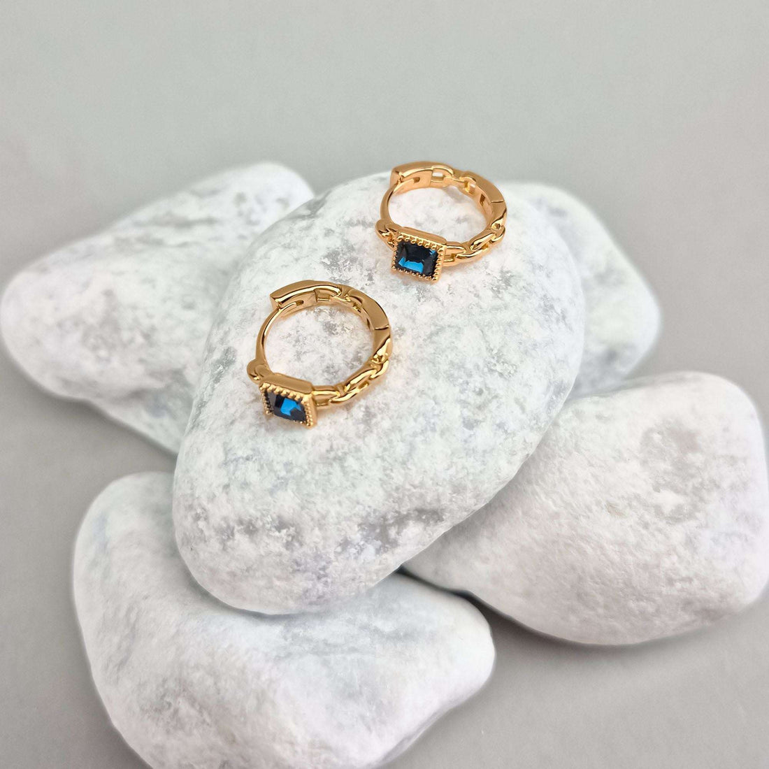 Gold-tone hoop earrings with a blue stone on white pebbles, chain texture in profile