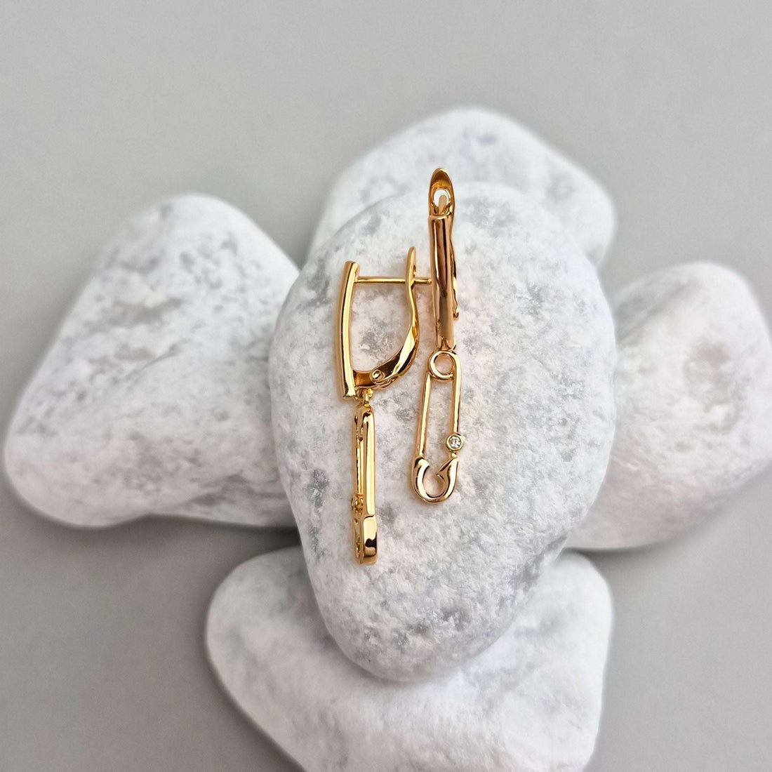 Gold-plated safety pin earrings on white stones, leverback clasp visible