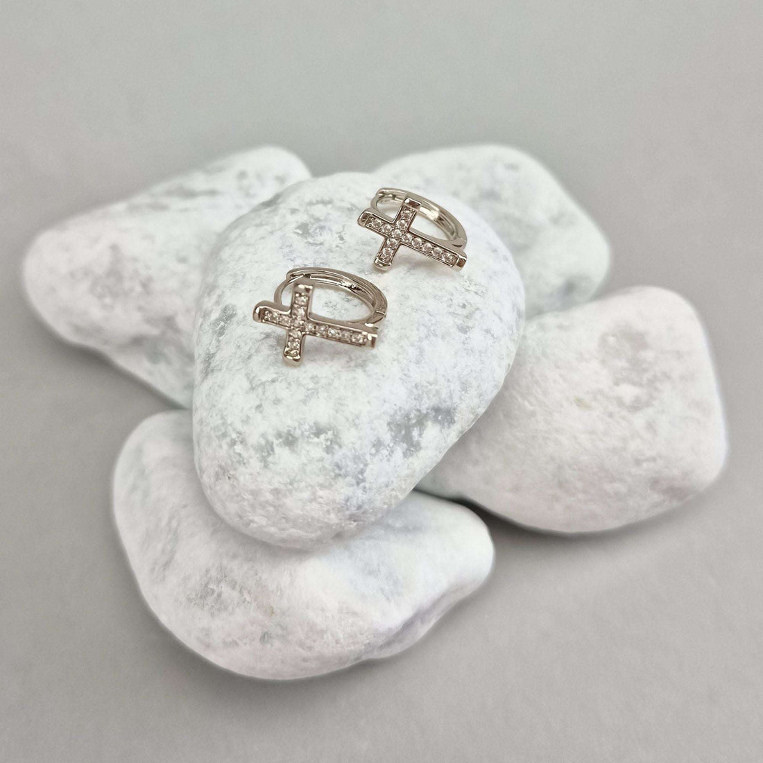 Close-up of silver-tone cross earrings with leverback clasps on white stones