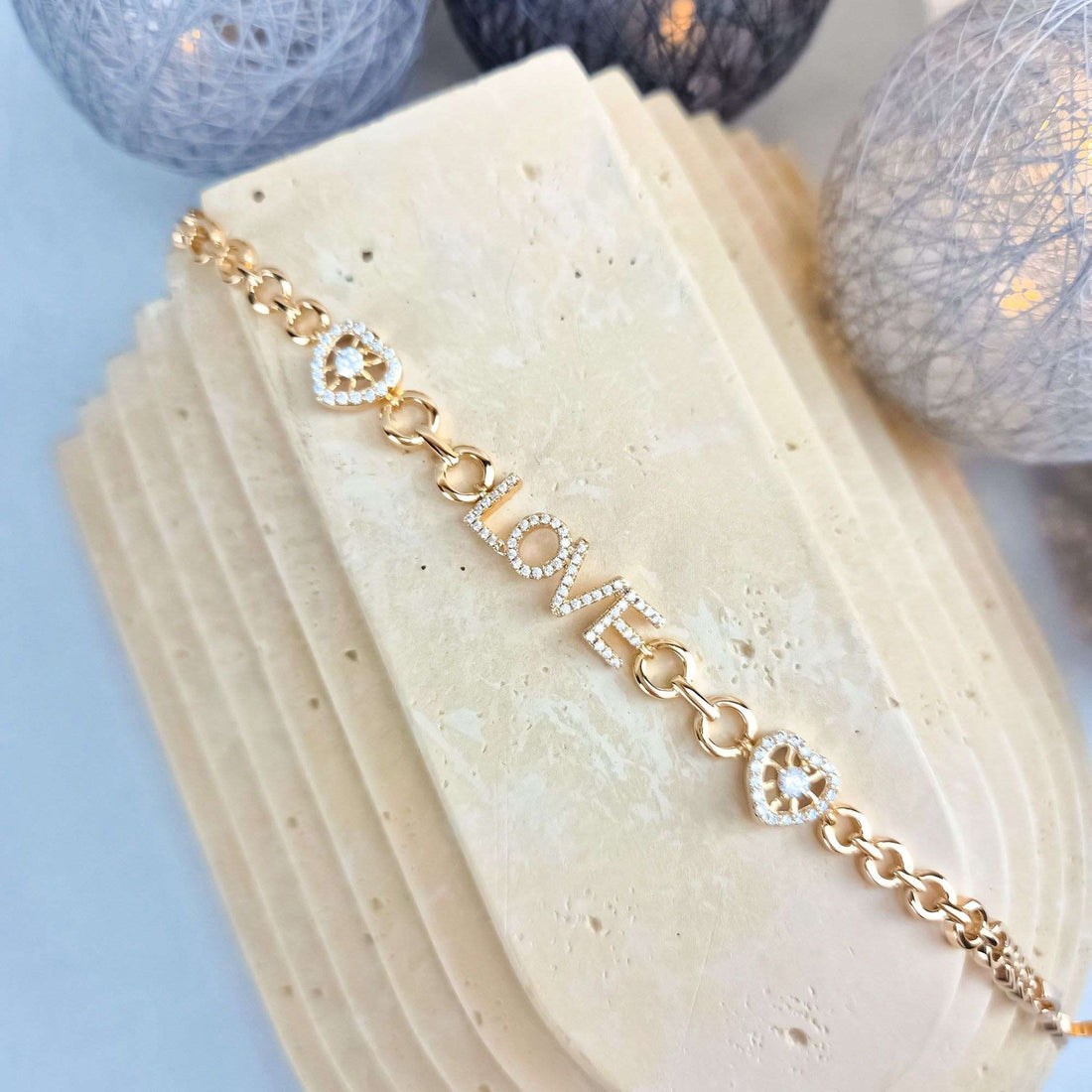 Gold-plated LOVE bracelet with cubic zirconia letters and hearts on a pale stone slab