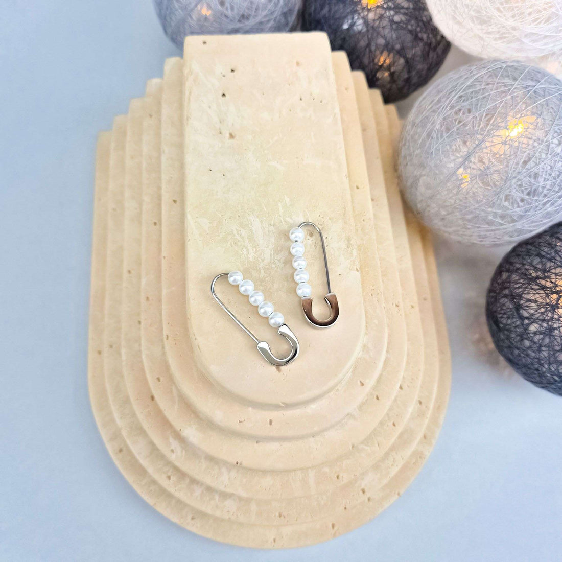 Safety pin earrings with white faux pearls on a pale stone stand