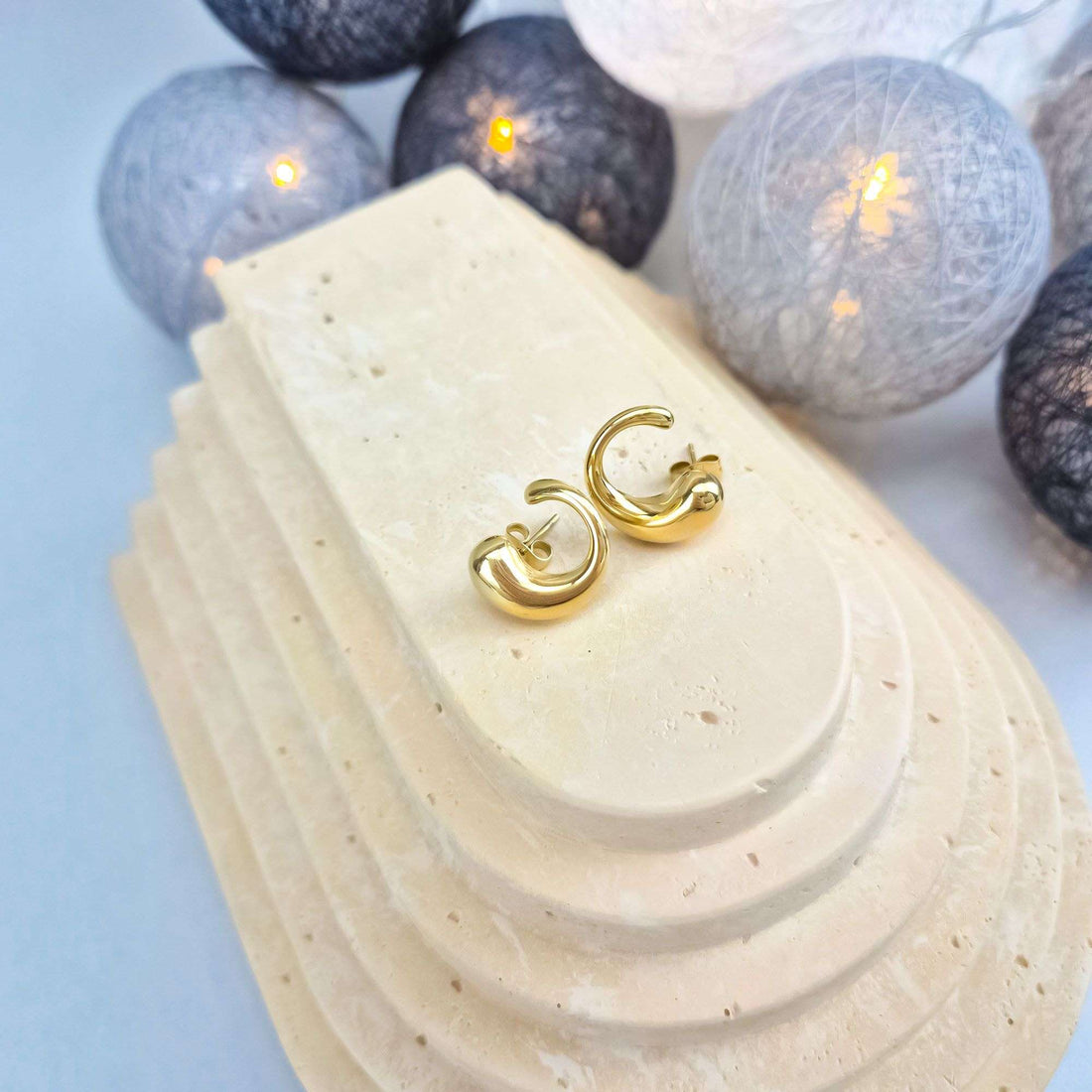 Chunky gold-plated half-hoop earrings with push-backs on a pale stone stand