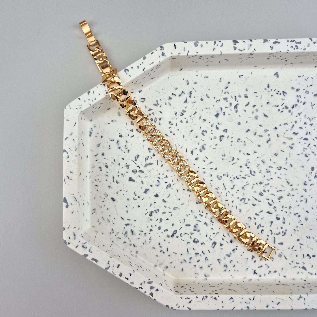 Gold-tone bracelet with sparkling crystals laid out on a white speckled ceramic tray